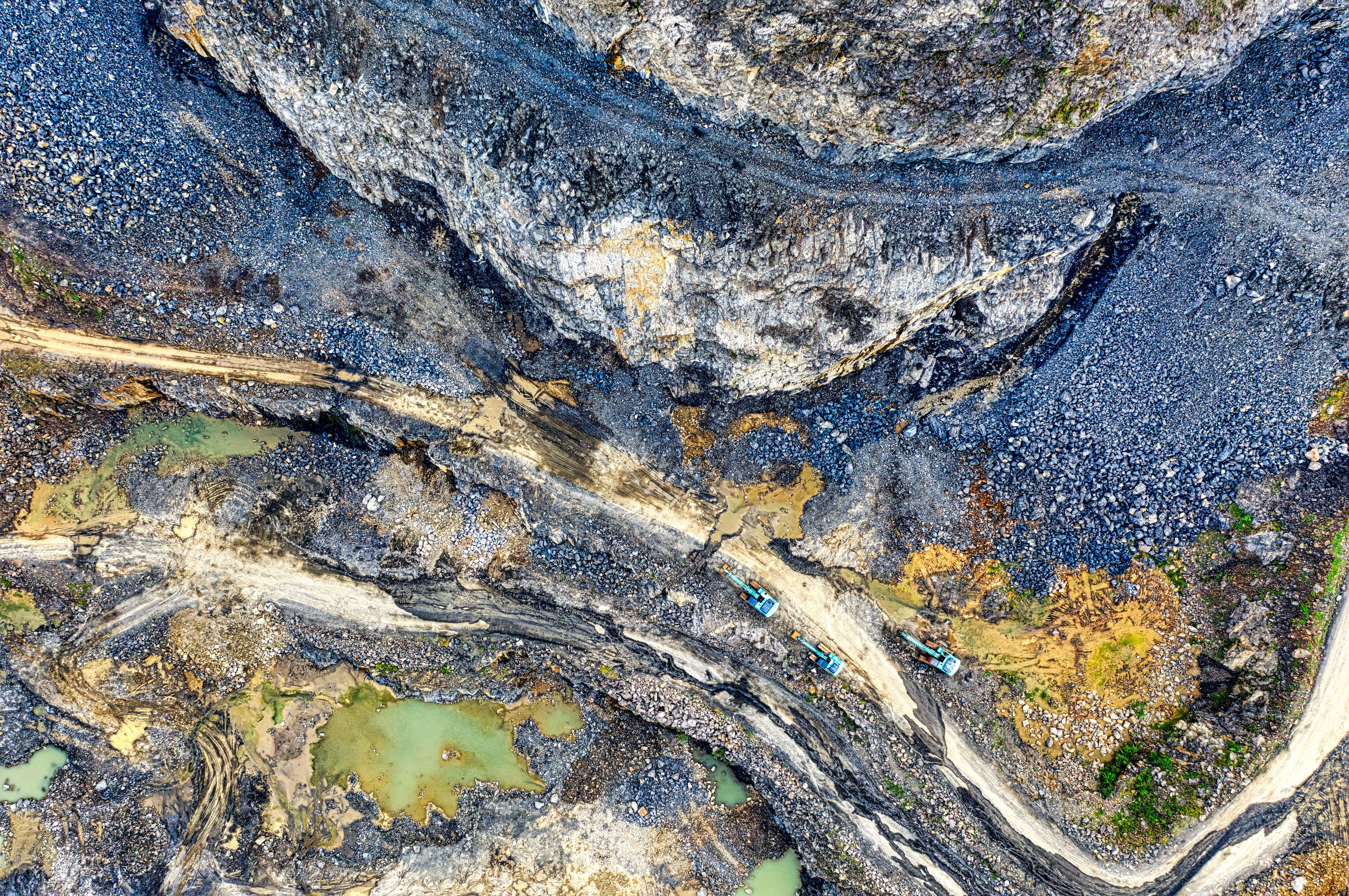 Looking straight down on an open-cut quarry: benched rock faces, haul roads and settling ponds.